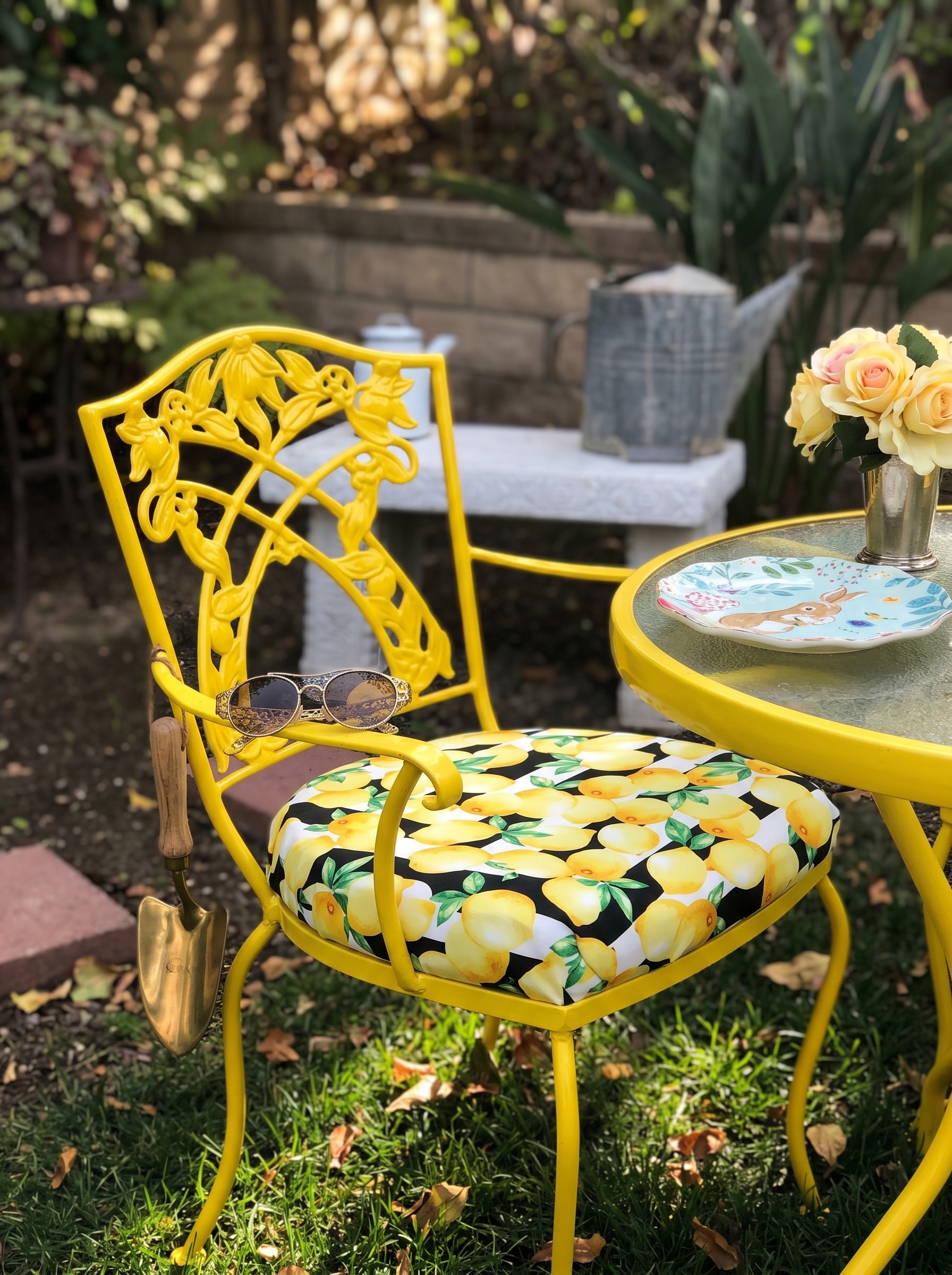 Colorful outdoor dining chairs with turquoise and yellow frames, floral cushions, rustic table, garden flowers, and string lights