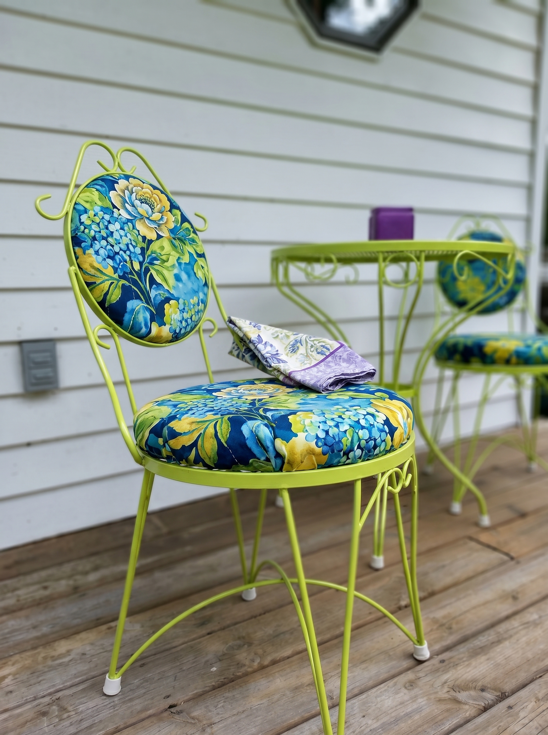 Pink metal outdoor dining chair with scrollwork backrest, matching table, purple flowers, gravel patio, and romantic garden cafe decor