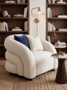 Deep blue armchair with geometric pillow, curved arms, black legs, floor lamp, wall art, side cabinet, and indoor plant