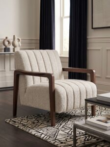 Oversized cream boucle armchair with rounded arms, wooden bookshelves, marble side table, gold wall lamp, and cozy reading nook decor