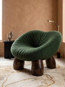 Minimal cream lounge armchair with green bolster pillow, boucle upholstery, rounded edges, wooden ball feet, and clean modern decor