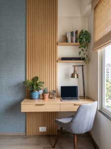 Modern L-shaped small home office with wooden desk, black storage cabinets, gray chair, wall shelves, window, and plants