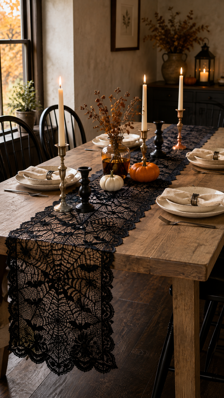Dollar Tree Halloween dining table with black lace spiderweb runner, ivory taper candles, brass candleholders, small pumpkins, amber vase, dried branches, layered plates, dark flatware, black chairs, and rustic farmhouse dining room